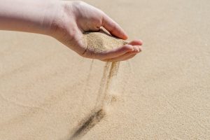 A hand pouring sand on a desert sand dune. Sand slips sifting through fingers