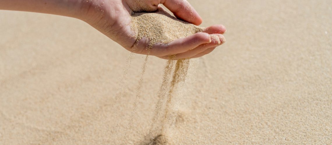 A hand pouring sand on a desert sand dune. Sand slips sifting through fingers